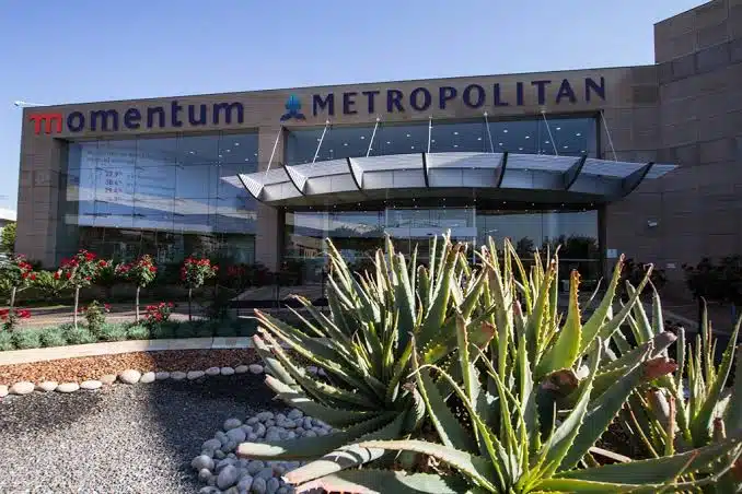 A large building in the background with bold text reading "Momentum Metropolis" displayed boldly on its facade. In the foreground, tall shrubs partially frame the view.