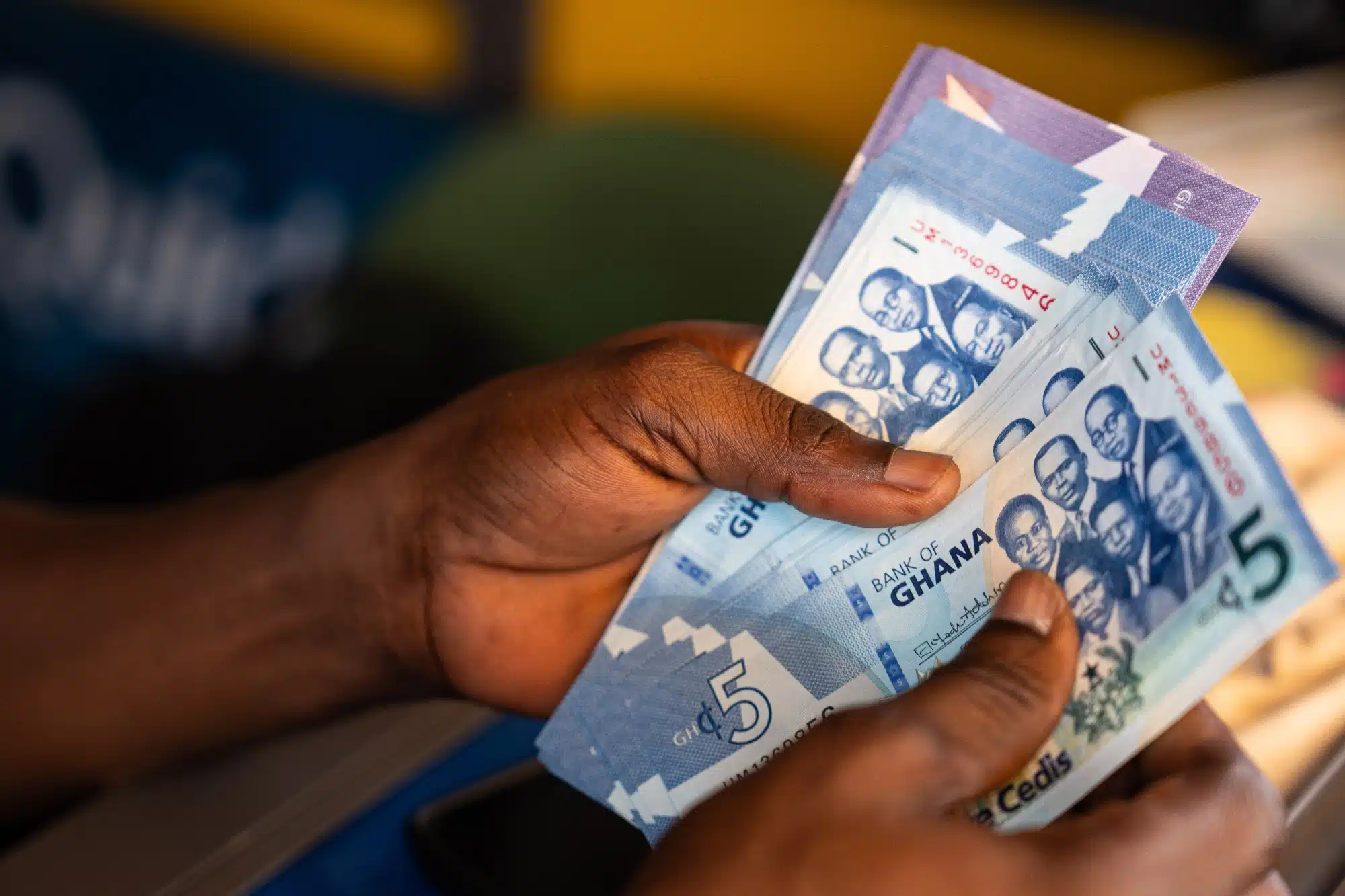 A hand holding and fanning out lower-denomination Ghana cedi banknotes, displaying their design and colours.