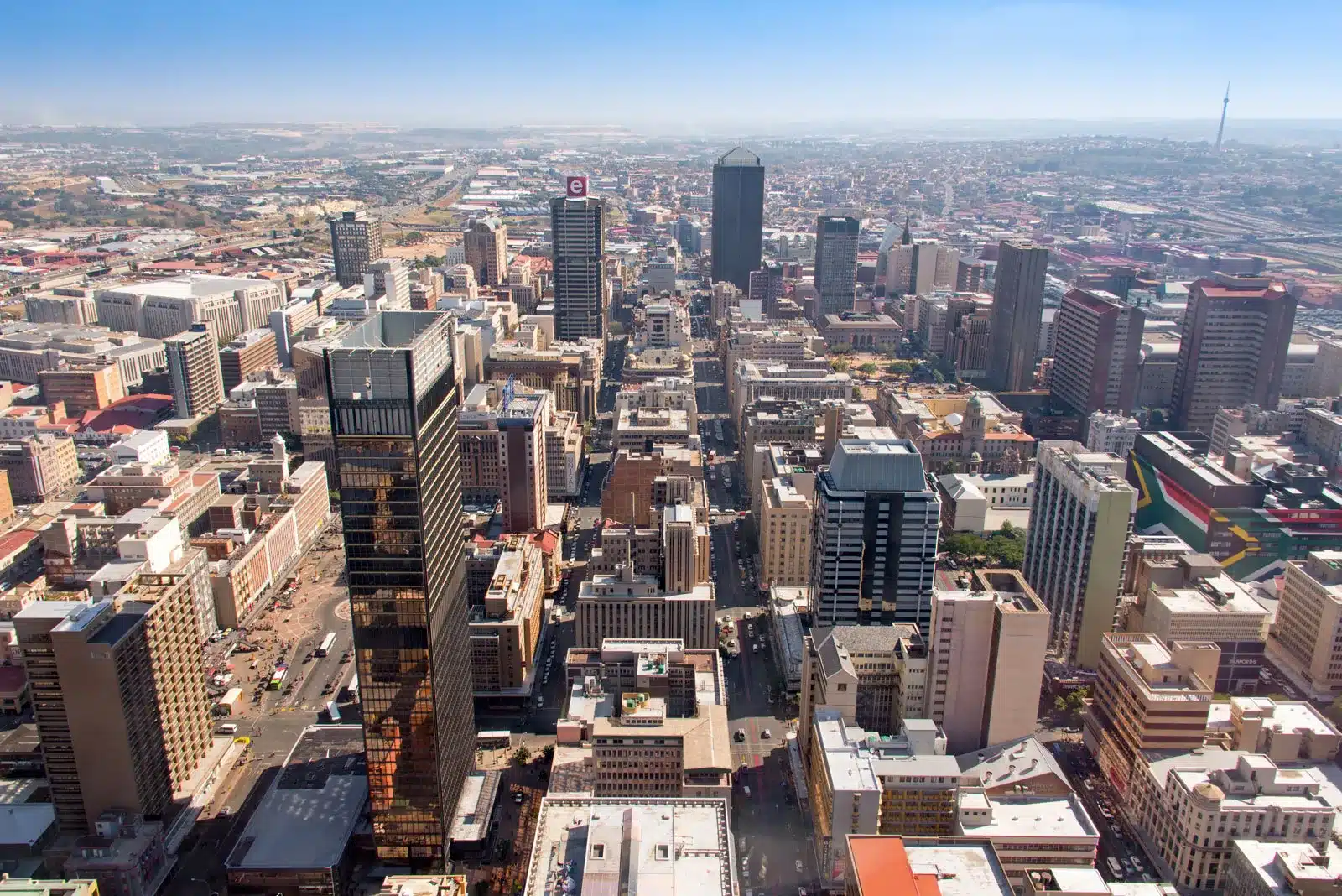 An aerial view of Johannesburg showcasing a dense cluster of high-rise buildings, with a mix of modern skyscrapers and older structures, capturing the city's bustling urban landscape.