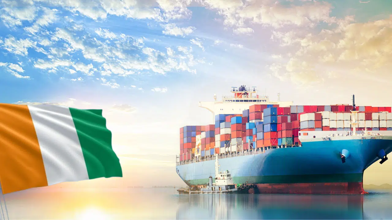 A cargo ship loaded with various sizes of freight containers, with the Ivorian flag superimposed on the image.