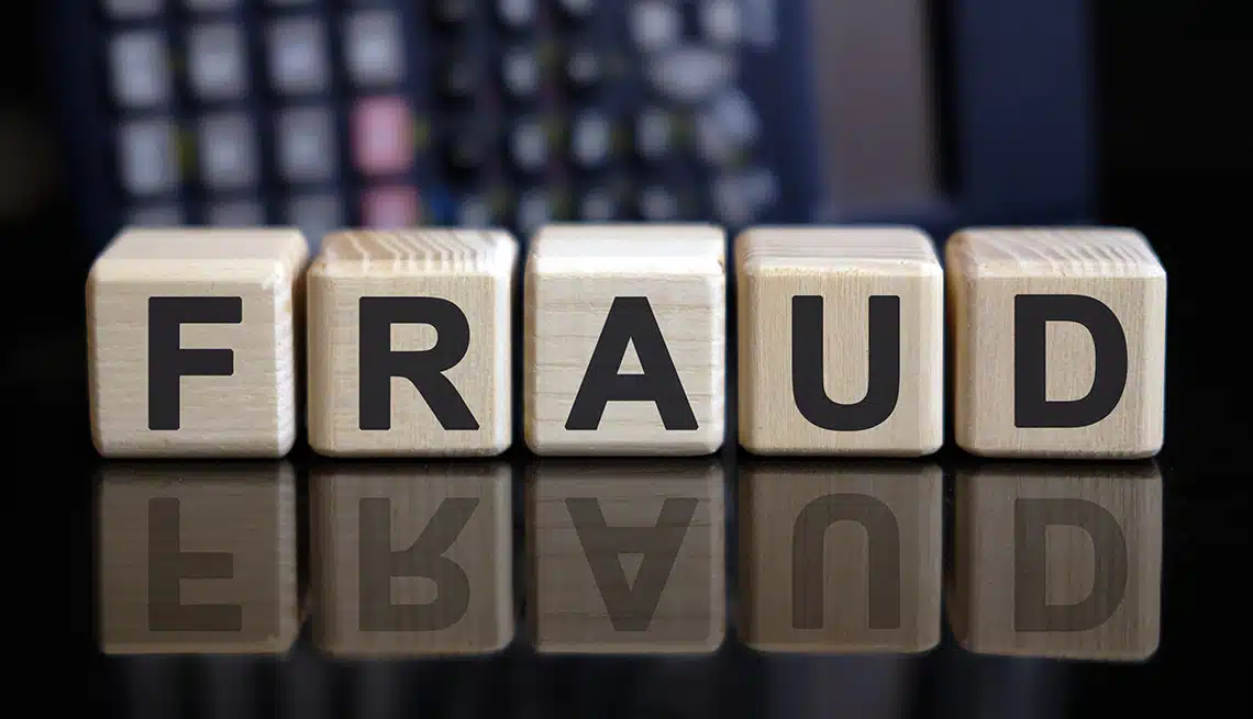 Wooden cubes with the word "Fraud" in bold letters, set against a blurry image of a calculator.