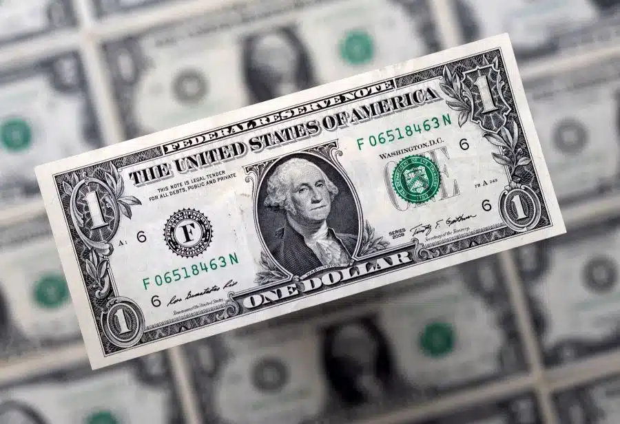 A dollar bill in focus with rolls of one dollar bills blurred to the background
