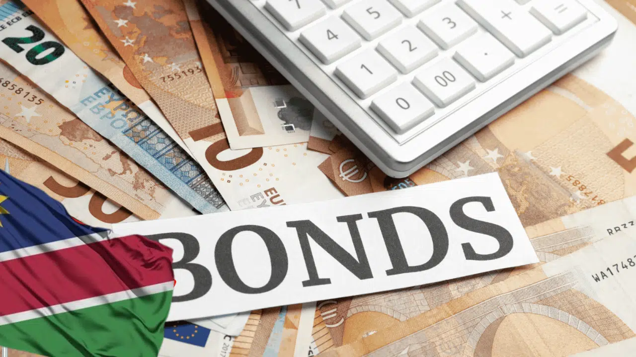 The Namibian flag superimposed on an image with the word “BONDS” spelt out on a white piece of paper — behind it is a calculator sitting on a spread of banknotes