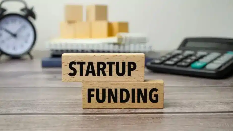 The image shows two wooden blocks stacked on top of each other with the words “STARTUP FUNDING” printed in bold black letters.