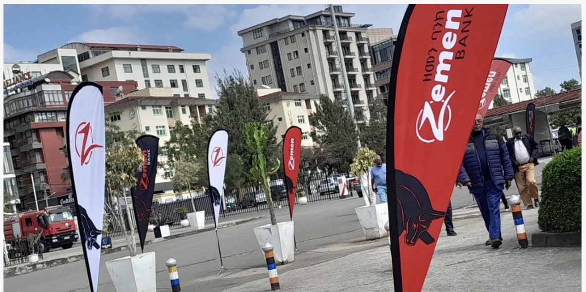 Several standing banners displaying Zemen Bank’s name, logo, and slogan, randomly placed on a pavement.